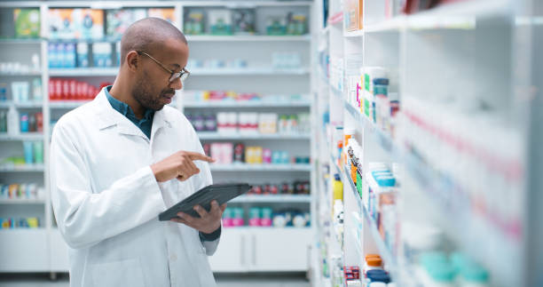istock Black man, pharmacist and checking stock with tablet on shelf for pharmaceuticals or inventory at pharmacy. Young African, male person or medical employee on technology at drug store or dispensary 2180482913