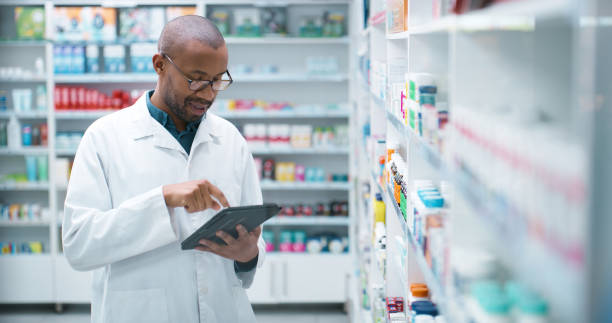 istock Black man, pharmacist and tablet with shelf for checklist, stock or inventory on pharmaceuticals at pharmacy. Young African, male person or medical employee on technology for healthcare at dispensary 2180482917
