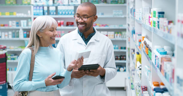 istock Pharmacist, helping and customer with pills, tablet and advice with pharmaceutical consultant. Shelf, question and mature woman with supplements choice and explain drug package directions in store 2180483021