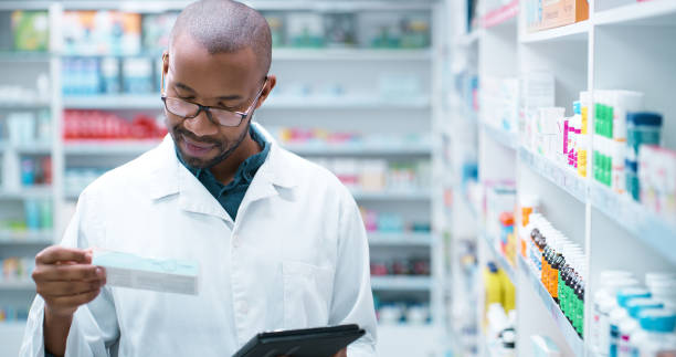 istock Black man, pharmacist and tablet with box for pharmaceuticals, inventory or side effects at pharmacy. Young African, male person or medical employee with technology or checking stock at dispensary 2180483108