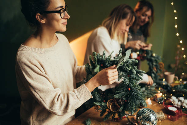 istock Happy women making Christmas wreath using natural pine branches and festive decorations. 2180483519