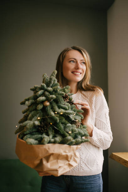 istock Young woman in white sweater holding small handmade Christmas tree. 2180483538