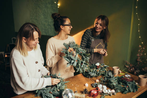 istock Happy women making Christmas wreath using natural pine branches and festive decorations. 2180483543
