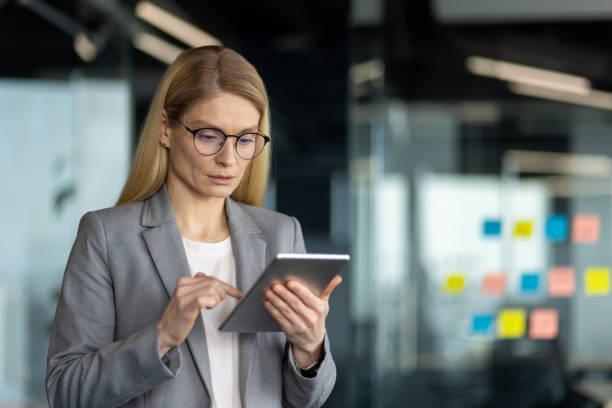 istock Professional woman in gray suit using digital tablet in modern office setting with focused expression, depicting efficiency and technology 2180484671