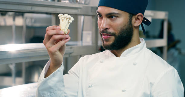istock Man, chef and mushrooms in kitchen at restaurant for thinking, cooking and culinary art with meal prep. Person, gourmet and edible beech fungus for diet, food or catering services with check at diner 2180491378