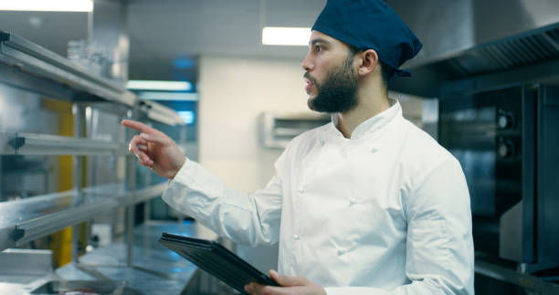 Chef, man and tablet in kitchen at restaurant with point, inspection and inventory with app at small business. Person, cook and digital touchscreen for check, thinking or catering at night in bistro