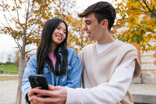 istock Multiethnic couple smiling and using smartphone outdoors in autumn 2180492536