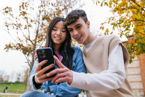 istock Young couple sharing a fun moment while looking at smartphone in a park 2180492568