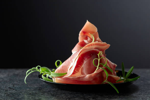 istock Italian prosciutto crudo with rosemary on a black plate. 2180494678