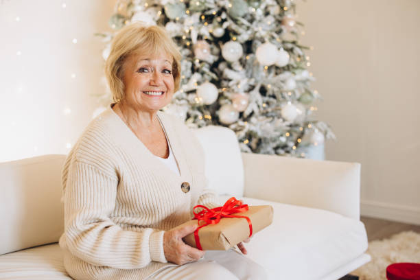 istock Happy Elderly Woman Holding Gift by Christmas Tree 2180498998