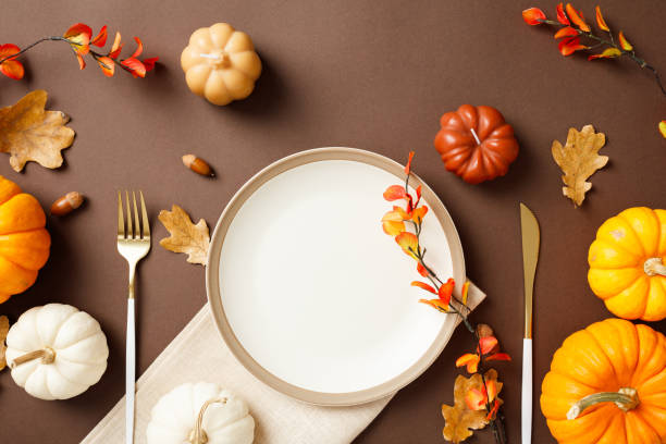 istock Autumn table setting with elegant white plate, golden cutlery, colorful fall leaves, pumpkins, and acorns on brown backdrop 2180501708