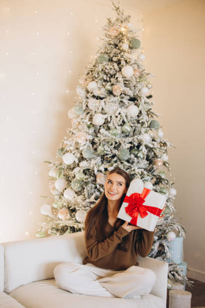 istock Woman Joyfully Holding Christmas Gift Beside a Decorated Tree 2180503660