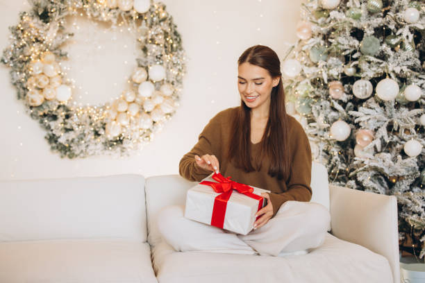 istock Woman Joyfully Opening Gift in Festive Christmas Setting 2180503692