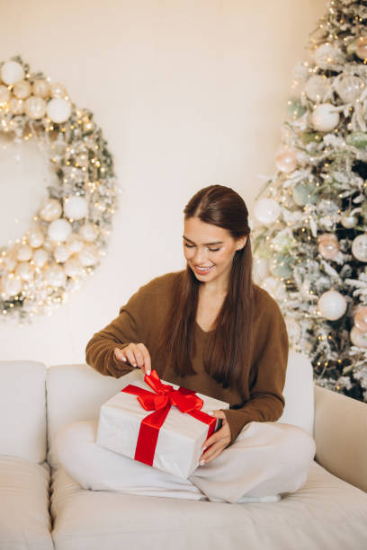 istock Woman Joyfully Opening Gift in Festive Christmas Setting 2180503693
