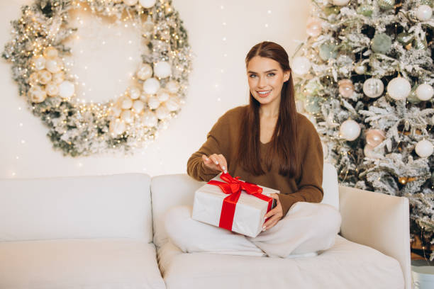 istock Woman Joyfully Opening Gift in Festive Christmas Setting 2180503741