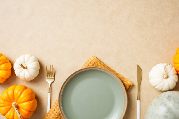 istock Autumn table setting with an empty plate, gold cutlery, and decorative pumpkins on a beige background 2180504594