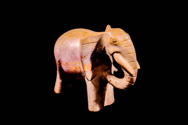 A small elephant statue is sitting on a black background. The statue is made of wood and has a brown color