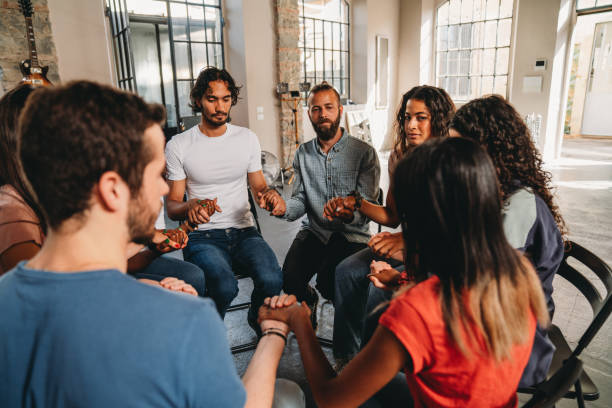 istock People are sitting in circle holding hands together during a group therapy session 2180506972