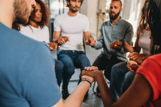 istock People are sitting in circle holding hands together during a group therapy session 2180506981
