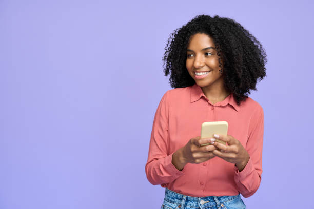 istock Young happy African woman using smartphone standing isolated on purple wall. 2180507784