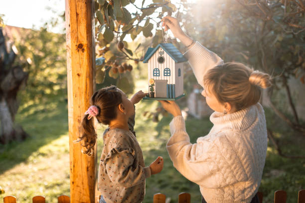 Mother and daughter hanging a birdhouse they made on a tree in back yard