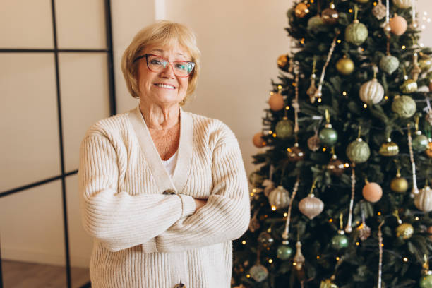 istock Smiling Senior Woman Standing by Decorated Christmas Tree 2180510488