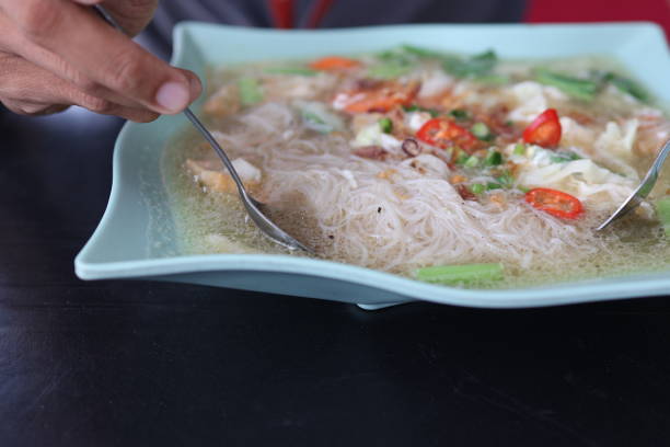 Close-up of a savory Asian rice noodle soup, garnished with fresh herbs, red chili slices, and vegetables. Perfect for culinary themes, food blogs, and recipe websites.