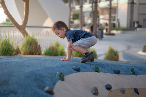 Energetic boy climbs a decorative rock path in an urban park, showcasing young adventurous spirit amidst the greenery and architectural backdrop of the modern city.