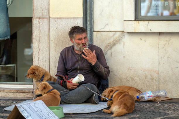 Lisbon, Portugal - September 8, 2024 : A man rests on the pavement with dogs while seeking assistance from passersby.