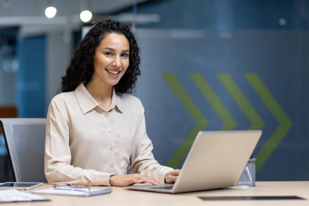 istock Confident Hispanic woman working on a laptop in a modern office setting, showcasing professionalism and productivity. Perfect for business concepts, teamwork, and office environment portrayals. 2180554067