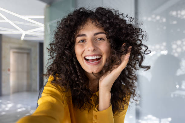 istock Smiling woman taking a video call selfie looking at camera using phone indoors in modern office setting 2180559055