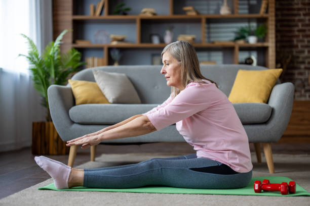 istock Senior woman practicing yoga at home, stretching while sitting on mat indoors. Promoting flexibility and healthy lifestyle in living room setting with comfortable decor 2180559215