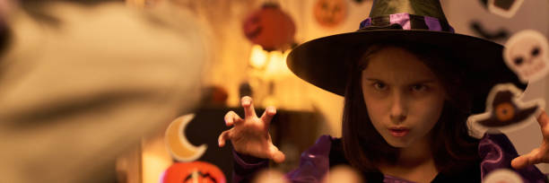 young girl with wich costume  celebrating Halloween party against plain background