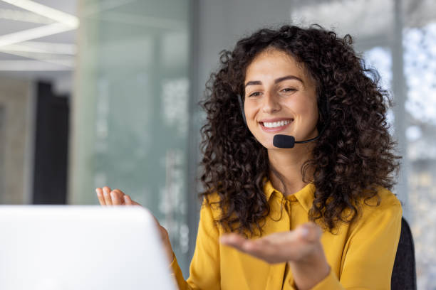 istock Hispanic businesswoman with curly hair smiling while working in modern office using headset for virtual meeting 2180563283