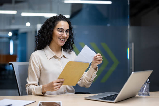 istock Cheerful hispanic woman in office opens envelope with a bright smile and enthusiasm, highlighting professional success and positivity during workday at modern office desk with laptop and phone 2180571490