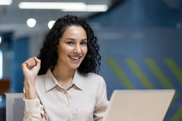 istock Confident businesswoman smiling with success gesture in modern office environment working on laptop 2180572119