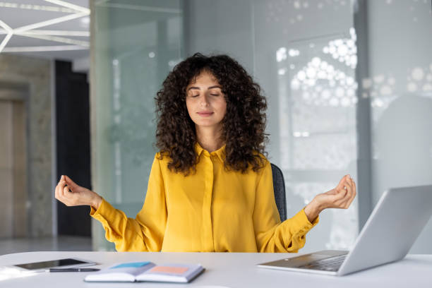 istock Woman in yellow blouse sitting at office desk practicing meditation and relaxation techniques for stress relief and focus 2180573375