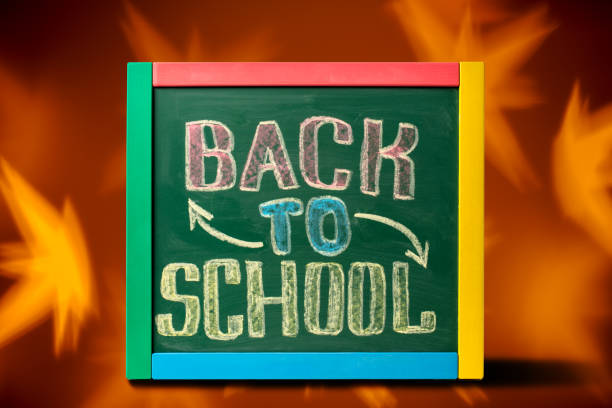 Blackboard with BACK TO SCHOOL lettering hand drawn by colorful chalk. Defocused autumn leaves background.