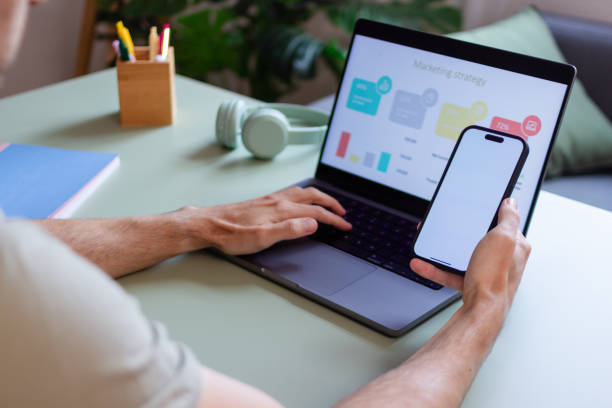 istock Marketing manager working on laptop and checking smartphone with blank screen 2180584687