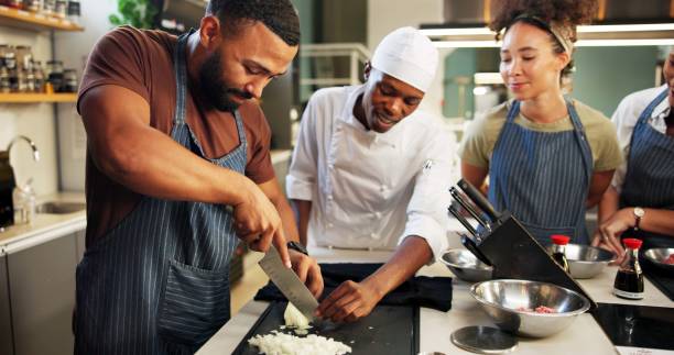istock Cooking, course and chef teaching man in kitchen for knife skills, cutting technique or learning process. Culinary class, people or mentor with lesson on onion preparation or education in hospitality 2180584723