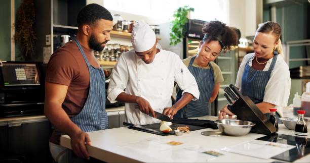 istock Cooking, class and chef teaching people in kitchen for knife skills, cutting technique and learning. Culinary course, students and mentor with lesson on onion preparation and education in hospitality 2180584729
