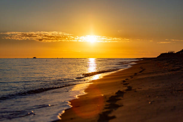 Golden sandy beach with fresh footprints in the sand with a sunrise and sea as the background.
