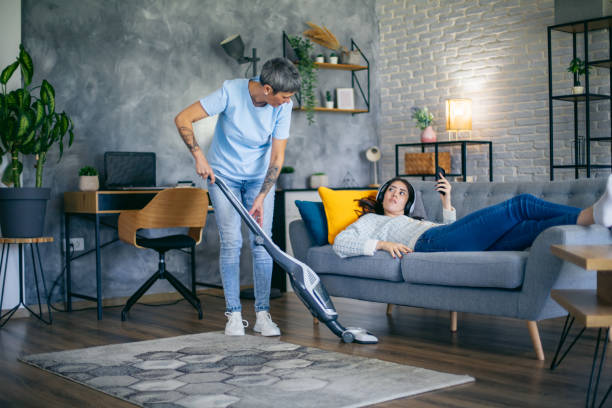 istock Mother cleaning with vacuum cleaner while daughter using mobile phone 2180592729