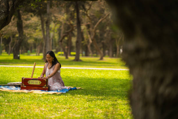 Woman sitting in park playing harmonium with her musical instruments next to her, wearing dress