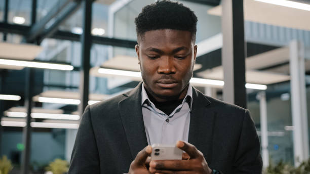 istock Serious young man african american office worker searching smartphone internet choosing making order chatting online with friends scrolling mobile phone thoughtful male user click at browser account 2180593897
