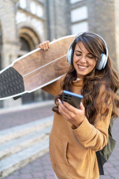 istock Caucasian skateboarder woman smiling while using her mobile phone outdoors on the street 2180598319