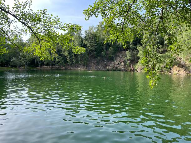 istock A serene lake surrounded by lush greenery with people swimming on a sunny day. 2180601888