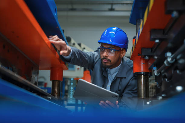istock Engineer with a blue helmet and safety glasses, checking manufacturing machinery 2180607174