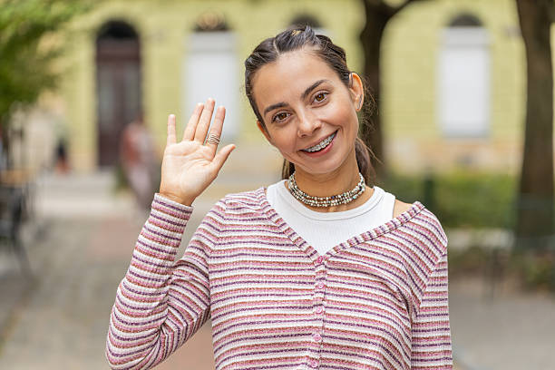 istock Happy woman smiling friendly at camera waving hands gesturing hello greeting goodbye on city street 2180615577