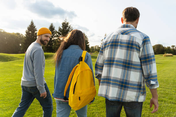 Three students are walking together on a green grass lawn on a university campus, enjoying the outdoors and each other's company